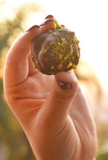 Persona sosteniendo un Mini Bonz de pistacho, snack dulce y salado cubierto de chocolate.
